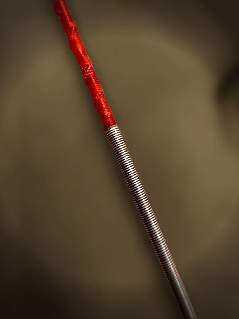 Macro photograph of a silk string with copper winding meeting a red silk wrap